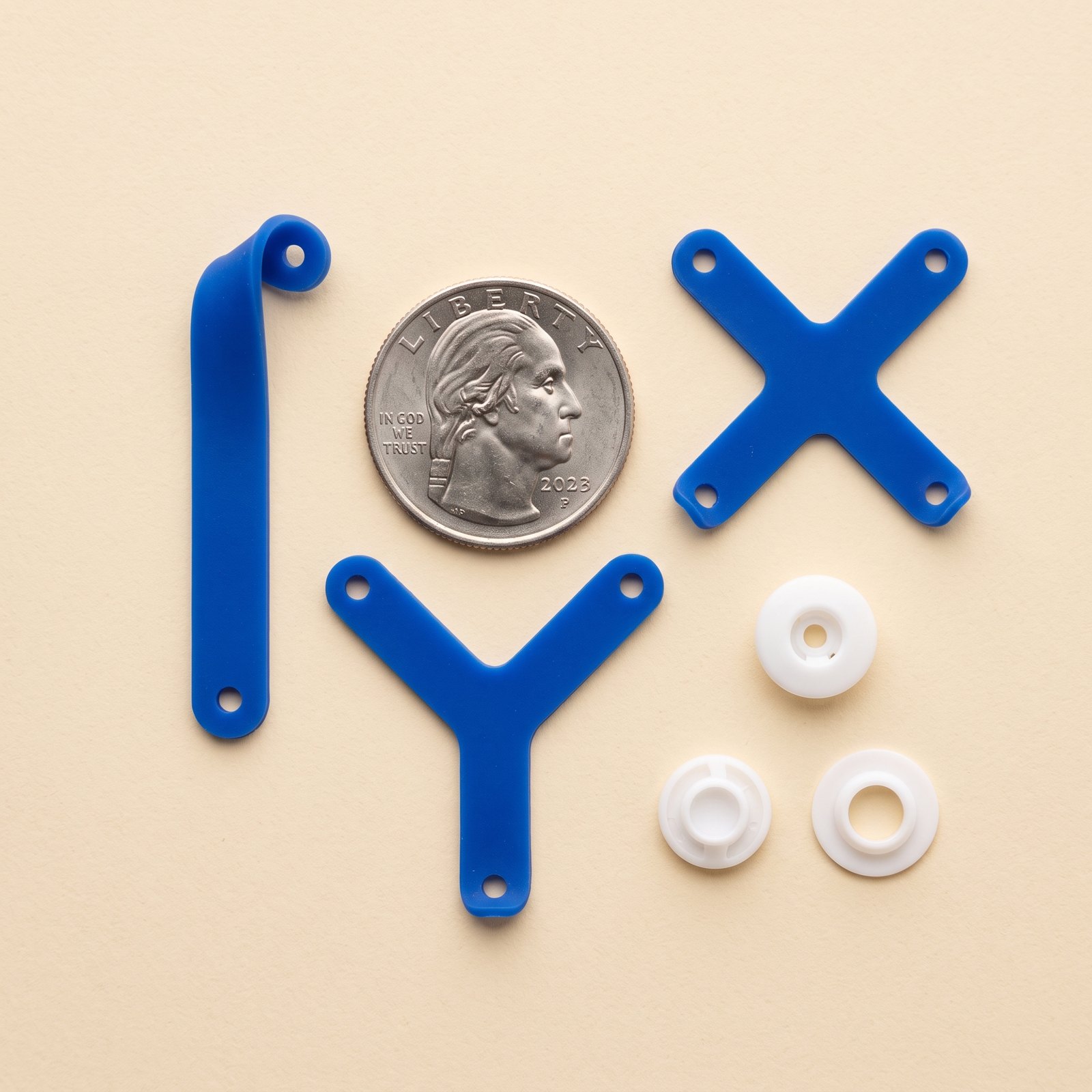 Three blue silicone mount pieces, a bar, a Y and an X, with three white snap holders and a quarter for scale